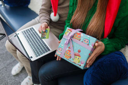 Close-up of a young couple on the couch, a man is holding a credit card and a laptop, a gift girl, online shopping.の写真素材
