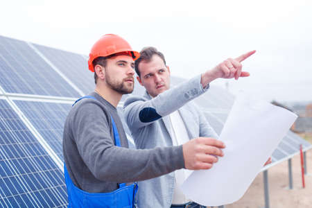 The chief with the worker keep the Whatman and look somewhere against the background of solar panels