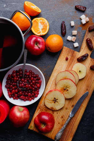 Slices of apples on a wooden board, sweet dates, near a deep white plate with juicy cranberries and a metal pan with compote. Indoors. View from above.の写真素材