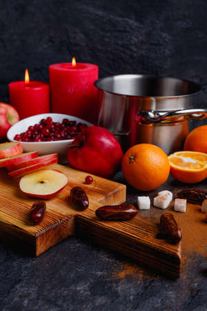 On the table is a board with apples and dates, a pan, oranges, cranberries and burning candles.の写真素材