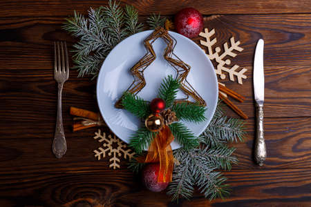 In a plate is a fir-tree, next to cutlery and branches of a fir-tree with balls, snowflakes and...