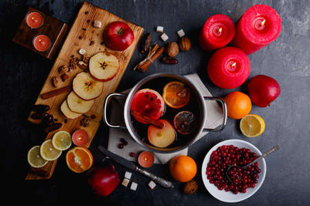 On the table is pan with mulled, a board with slices of apples and lemon, a plate with cranberries and candles.の写真素材