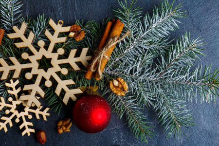 Close-up tree branch with snowflakes, a tree toy, a cinnamon stick and walnuts. On a dark background.の写真素材