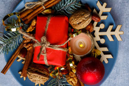 On a plate is a small gift box, a burning candle, walnuts and cinnamon sticks.の写真素材