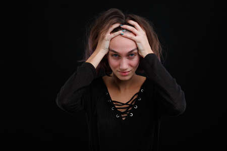 A girl in a black sweatshirtwith a cunning look is holding her head.の写真素材