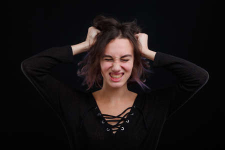 The frustrated girl clasped her hands behind her hair. On a black background.の写真素材