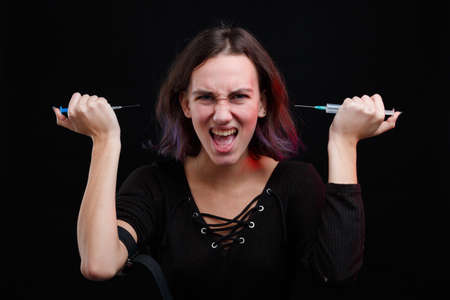 A drug addict holds two syringes in her hands and screams. On a black background.の写真素材