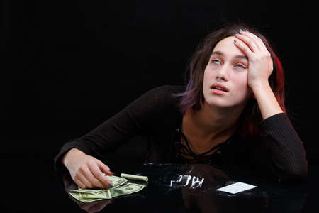A drug addict under the narcotic effect of cocaine sits at a table. On a black background.の写真素材