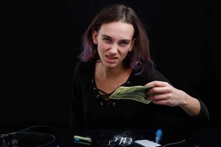 A drug addict aggressive girl holds money in her hands. On a black background.の写真素材