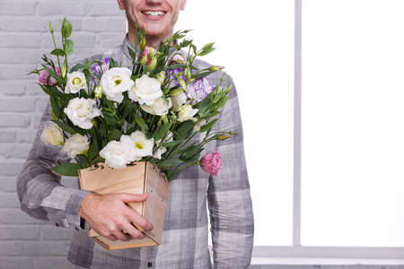 A guy is holding a flower pot with roses on a white background. Front viewの写真素材