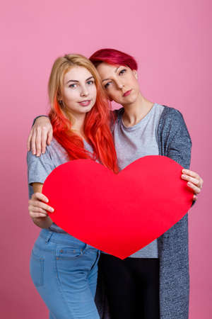 Lesbians are holding a heart in a hug on a pink backgroundの写真素材