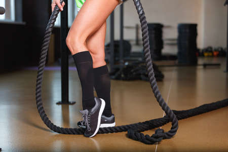Close-up of a girl's legs in the gym, with a black big rope, view from the side.