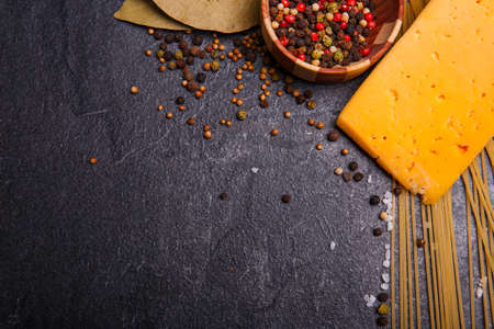 Close-up of cheese, spices, spaghetti on a black concrete background, sprinkled with pepper peas, cooking Italian food, free space for text.の写真素材