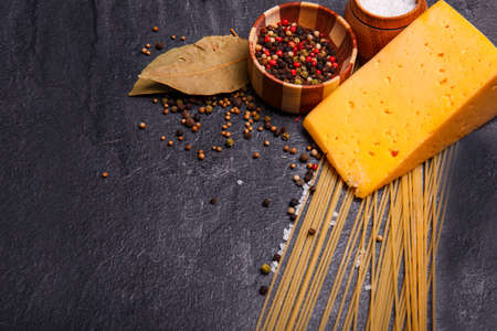 Close-up of cheese, spices, spaghetti on a black concrete background, sprinkled with pepper peas, cooking Italian food, free space for text.の写真素材