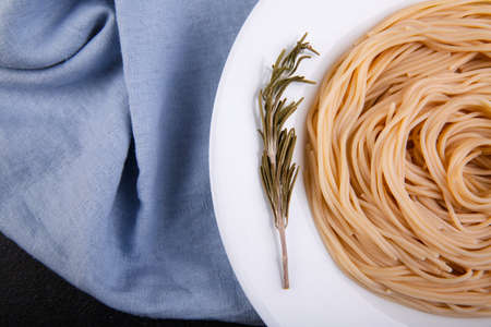 Close-up of a spaghetti of hard varieties in a white plate, with a sprig of sweep, stands on a blue cloth, top view.の写真素材