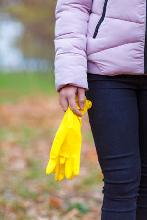 Close-up of a girl in an autumn park, outdoors, stands with rubber, yellow gloves in her hands, to harvest the fallen leaves.の写真素材