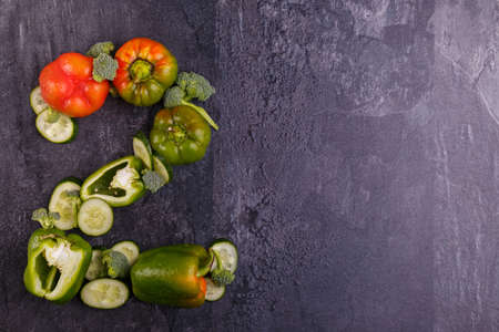 Close-up of appetizing vegetables, laid out in the number two, on the left side, Bulgarian pepper green and red, cucumber and broccoli slots on a black background, free space for text.の写真素材