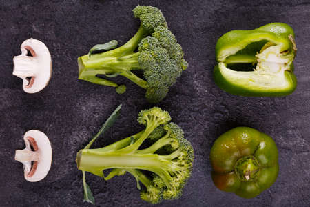 Close-up of champignons, broccoli and bell pepper are spread out on a black background, lie in horizontal position, password-protected to each other. Macro photography.の写真素材