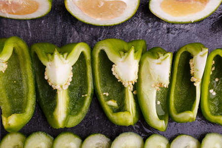Close-up of sliced, appetizing, healthy vegetables on a black background. Bulgarian pepper, cucumbers, and lime slices.の写真素材