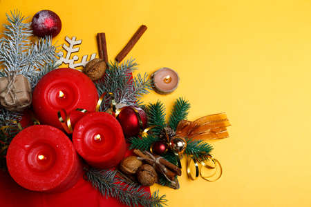 On a yellow background in the lower left corner is a Christmas composition, three red candles, cinnamon, toys for a Christmas tree, spruce branches, free space for textの写真素材