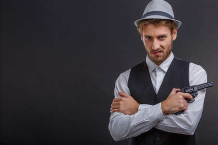 Gangster folded his arms over his chest with a gun on the left on a gray backgroundの写真素材