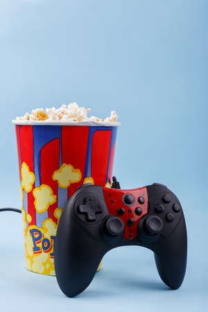 Joystick black with a red center stands at the bowl with popcorn on a blue backgroundの写真素材