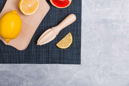A wooden anchor on which a lemon on a dark towel and a juice squeezing tool with a grapefruit slice close-up in the upper right corner on a gray background. View from aboveの写真素材