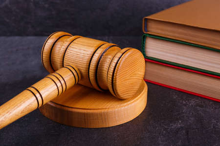 The judge's wooden hammer lies on the stands next to a stack of books of different colors on a stone background. Side viewの写真素材