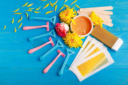 Set for depilation with strips, razors multi-colored, wax, chopsticks and cassette with wax on a blue wooden background. Top view of a closeupの写真素材