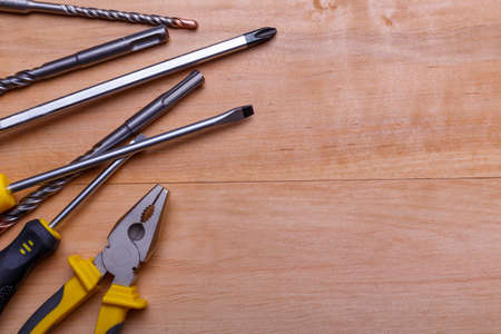 Tools are different screwdrivers, pliers and drills of different diameters are shown not fully in the left side on a wooden backgroundの写真素材