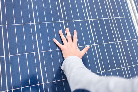 The hand of the European man lies on the panel of a modern solar battery. Outdoors.の写真素材