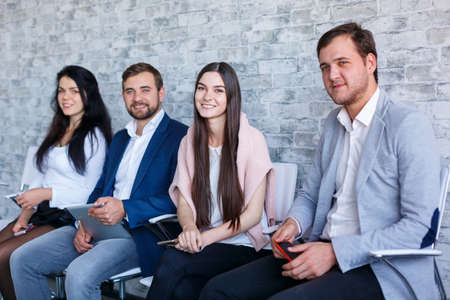 A group of happy people, sitting and smiling, holding mobile phones and a tablet. Indoors.の写真素材