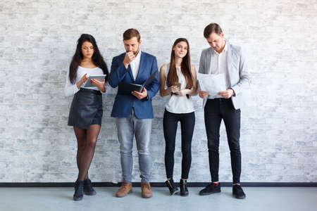 The guys and a girl are standing and holding document, folder, a tablet and phones. Indoors.の写真素材