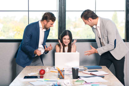 Two men viciously yells at the girl, the girl cries and hides her hands. Inside the office.の写真素材
