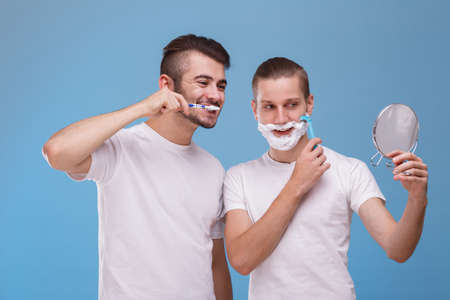 Two men look after themselves. One cleans his teeth, and the second shaves his beard.の写真素材