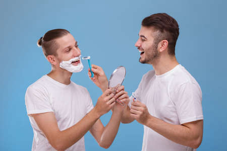 One guy shaves beard to another. On a blue background.の写真素材