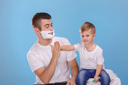 A guy with a foam on his face holds the hand of a small boy. On a blue background.の写真素材