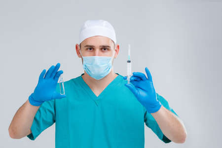 A doctor in uniform, mask and gloves is holding a ampoule and a syringe. Isolation.