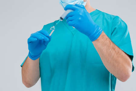 The doctor in form and gloves gathers a medicine from a ampoule into a disposable syringe. Isolation.の写真素材