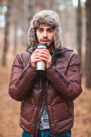 A handsome man i is drinking tea from a hot mug with a forest. Outdoors.の写真素材