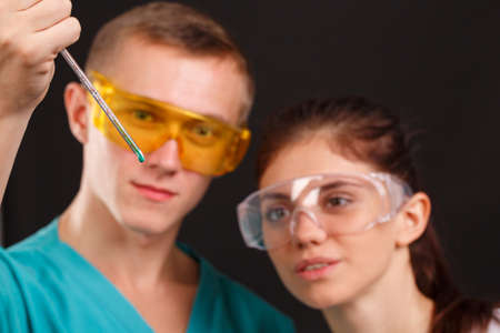 Two lab technician are holdings and looking at a measuring pipette. Indoors. On a black background.の写真素材