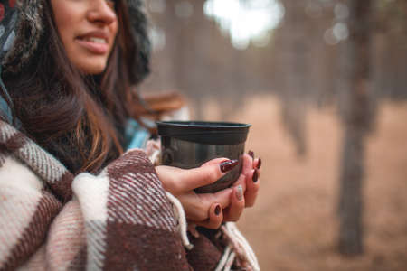 A girl is covered with a rug holding a cup with tea standing in a forest.の写真素材
