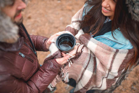 A couple holding on to a mug with tea. Outdoors in a forest. View from above.