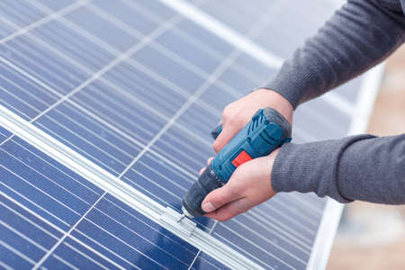 The hands of the solar battery station worker drills the panel. Close-up. Outdoors.
