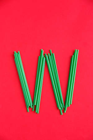 The letter W on a red background is laid out of green plastic cocktail tubes.の写真素材