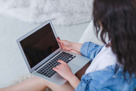 Girl working with laptop on her lap sitting by the bed on a white backgroundの写真素材