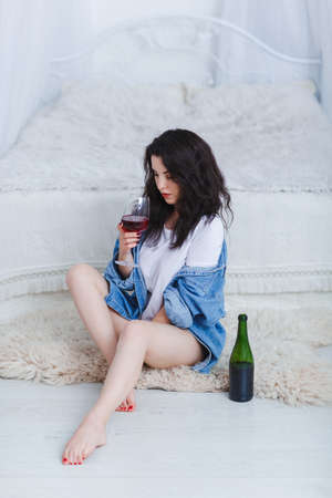 A girl sits by the bed with a glass of wine on a white backgroundの写真素材