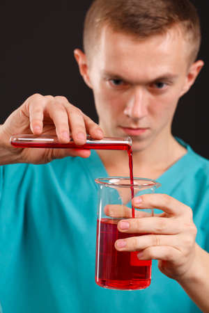 A man scientist pours liquid from a test-tube into another dish on a black backgroundの写真素材