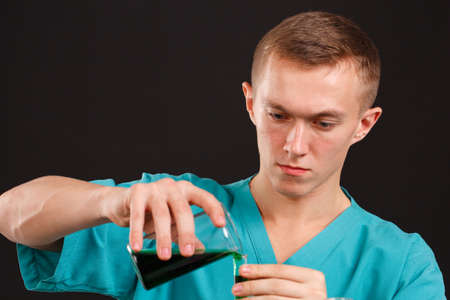 Man scientist pouring liquid in a flask into a test tube close-up on a black backgroundの写真素材