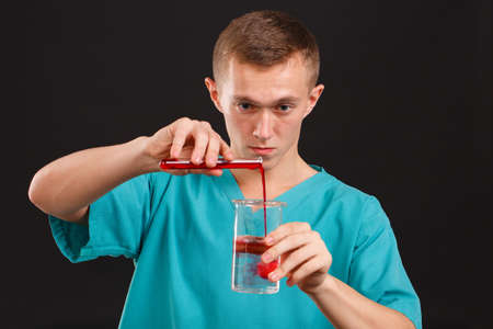 Man scientist pouring liquid from a test tube into a flask close-up on a black backgroundの写真素材